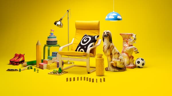 Fotoliu IKEA galben cu pernă decorativă, înconjurat de obiecte colorate – cărți, jocuri, role, jucării și lămpi – pe fundal galben intens, sugerând un colț de relaxare vesel și creativ.