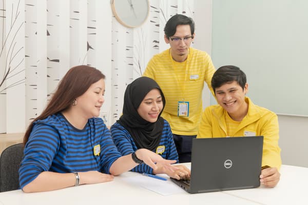 Four co-workers discussing a topic with smiles in front of a laptop. 