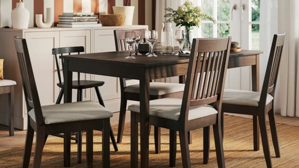 Four dark brown NÄSINGE chairs with light beige cushions are arranged around a black table in a stylish dining area.