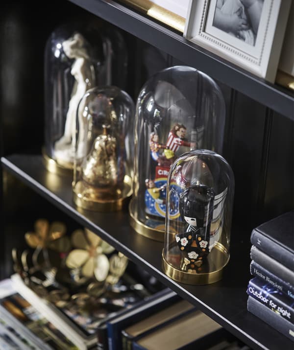 Four glass domes on a shelf containing various figures and ornaments.