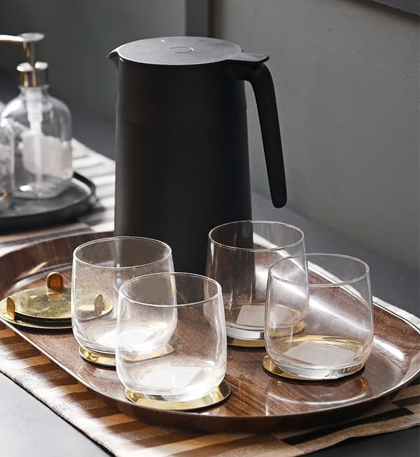 Four glasses and a black jug on a wooden tray.