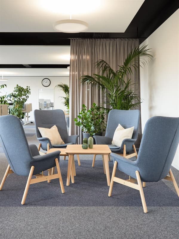 Four grey armchairs around a light wood coffee table with plants; grey curtains and a wall clock in the background.