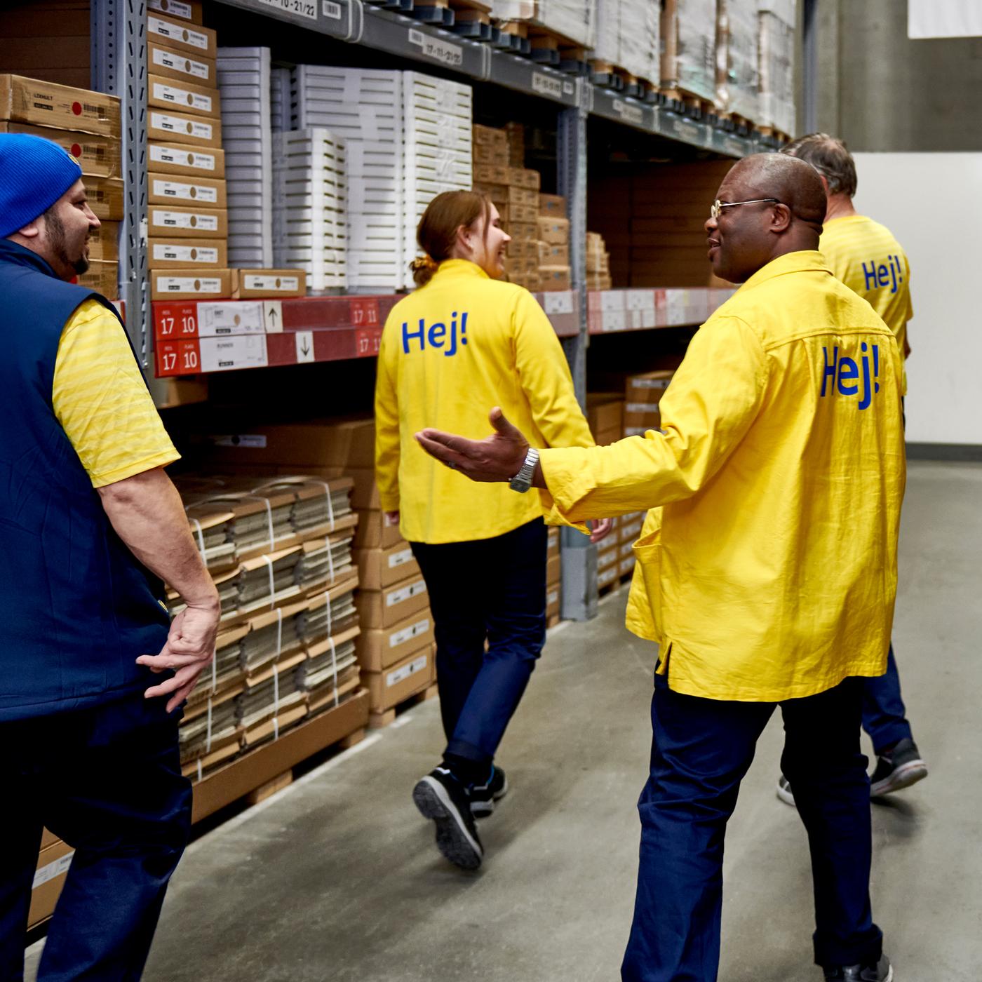 Four IKEA co-workers, three wearing yellow t-shirts and one wearing a blue vest, in the self-service area of an IKEA store.