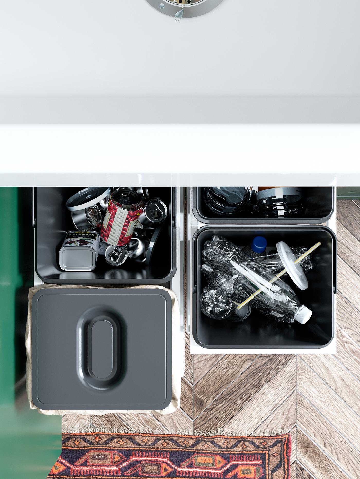 Four IKEA VARIERA black waste sorting bins filled with empty plastic bottles and cans. One bin has a lid on top.