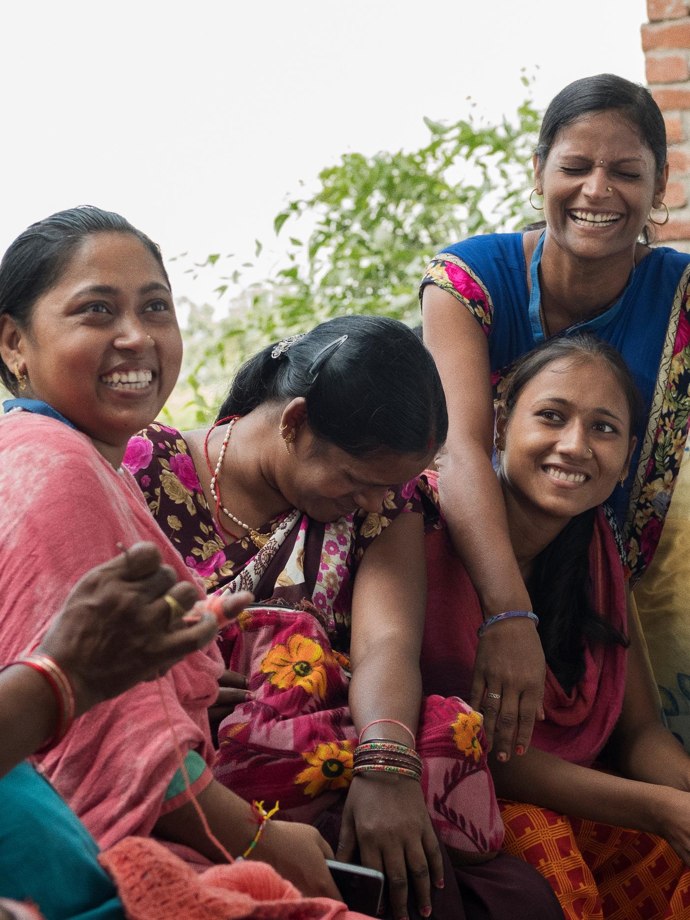Four Indian weavers in brightly coloured traditional dress and jewellery, enjoying a laugh outside.