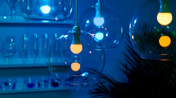 Four JAKOBSBYN pendant lampshades in glass with dimmable TRÅDFRI LED bulbs hanging at different heights in a dimly lit room.