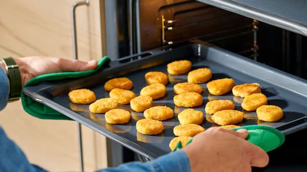 Four ouvert où l'on y voit une plaque de cuisson où se trouvent des galette de pommes de terre décongelés