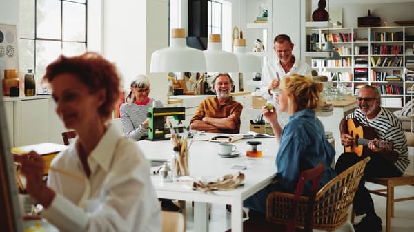 Four people around four white MELLTORP tables, below three BUNKEFLO pendant lamps.