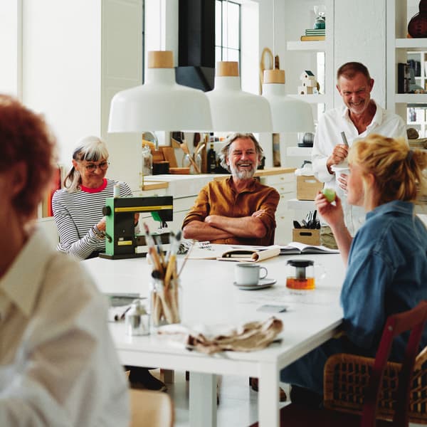 Four people around four white MELLTORP tables, below three BUNKEFLO pendant lamps.
