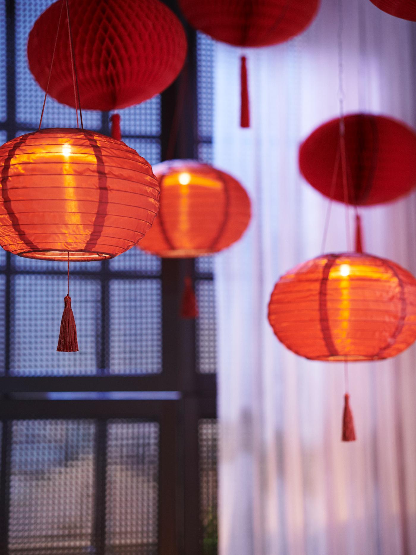 Four red FÖSSTA decorations and three lit FÖSSTA LED pendant lamps hanging in front of white drapes.