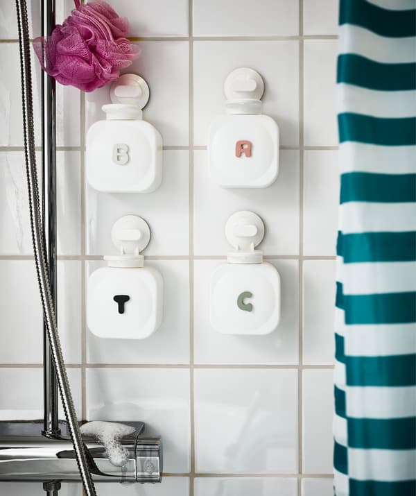 Four soap dispensers attached to white tiles next to a shower, with family member initials indicating ownership.