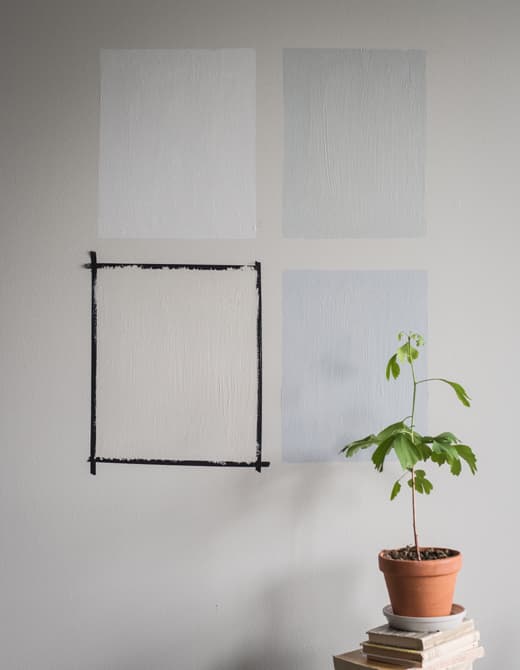 Four squares of different pain colours are painted onto a grey wall.