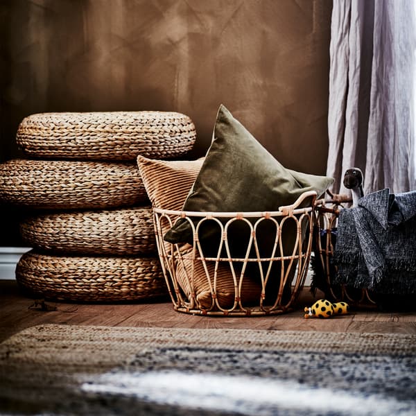 Four stacked stools made from banana fibre, two rattan baskets with pillows and a throw, a jute rug and a linen curtain.