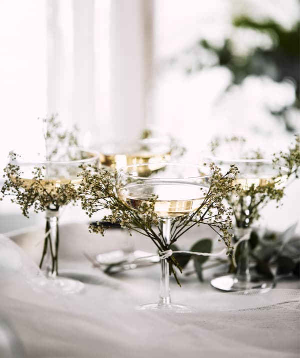 Four STORHET champagne coupes on a tray with tiny branches of small, wild flowers tied to the glass stems.