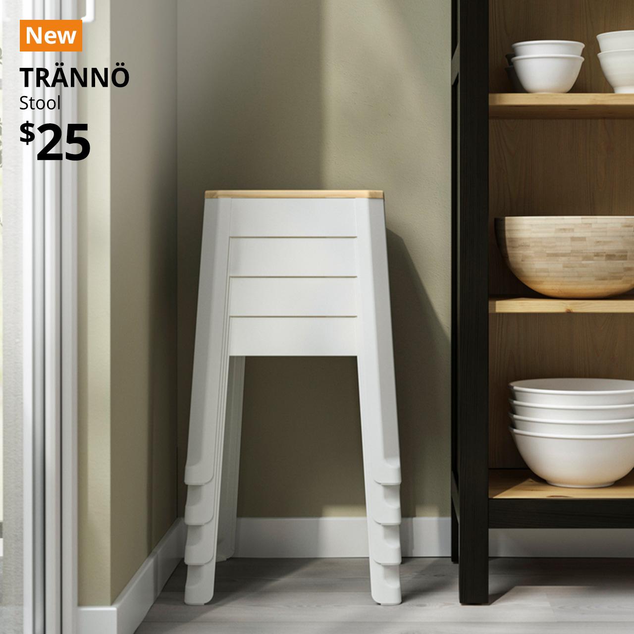 Four white/beige TRÄNNÖ stool is stacked and placed next to a shelving unit. A orange with white text that reads "New". Text on image reads "TRÄNNÖ, Stool, $25"