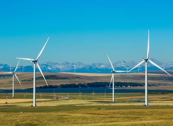 Four wind turbines in a green field with mountains and a blue sky in the background.