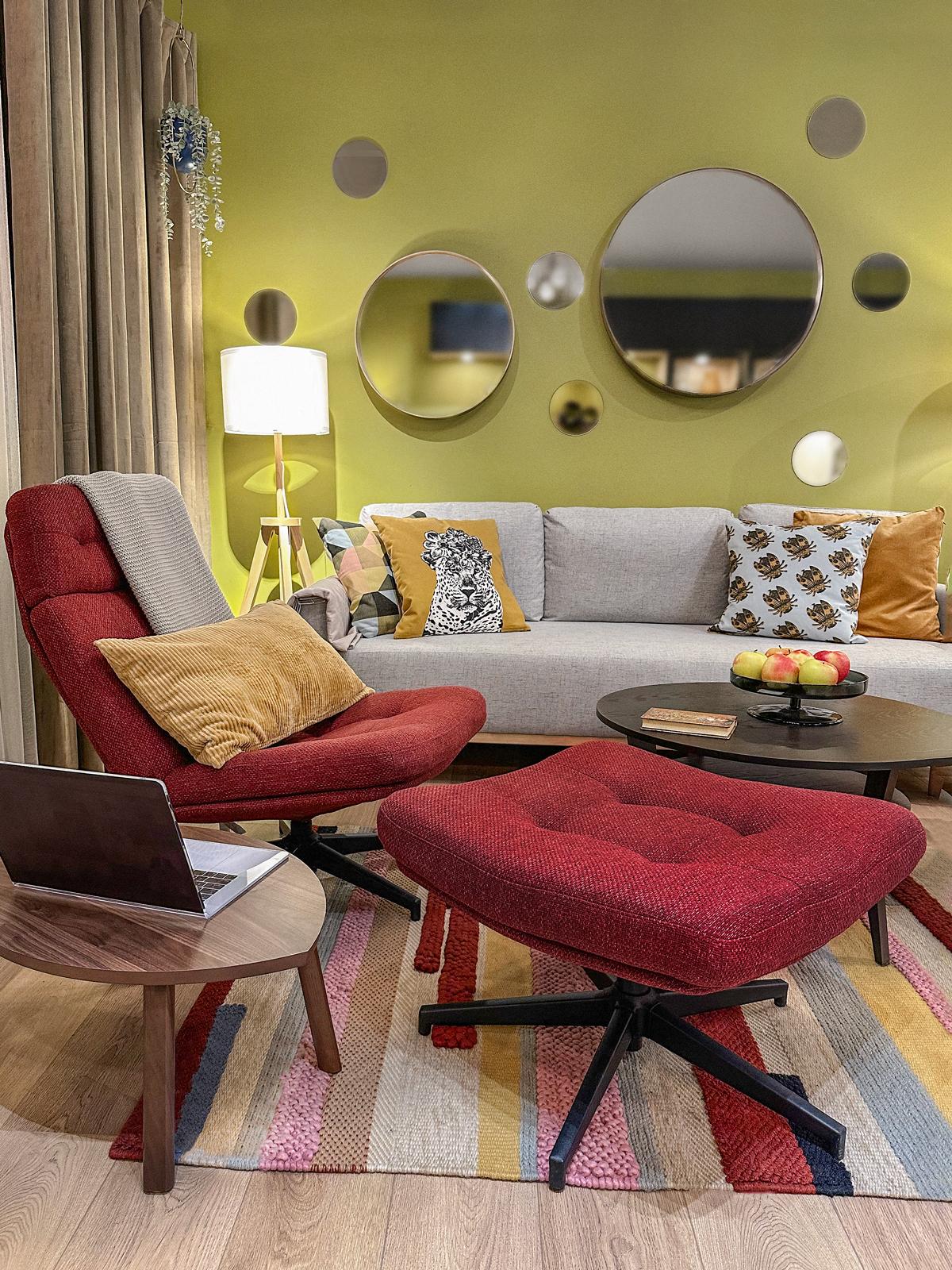 Fragment salonu. szara kanapa na tle zielonej ściany. Przed sofą znajduje się czerwony fotel z podnóżkiem. 