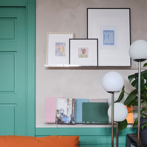 Framed art and posters, books and pastel-coloured notebooks are displayed on wall-mounted transparent picture ledges.