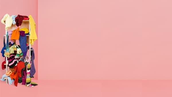 Framför en rosa vägg står en garderob där kläder ligger i en enda röra.