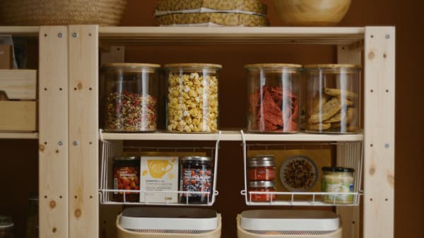 Frascos de vidro com alimentos conservados e frascos em cestos metálicos numa estante de madeira.
