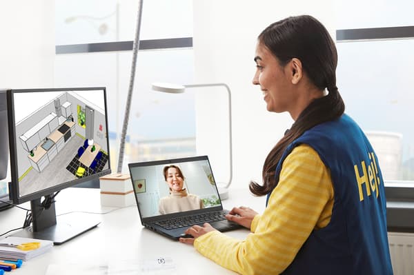 Frau sitzt vor zwei Bildschirmen und führt einen Videocall mit einer anderen Frau.
