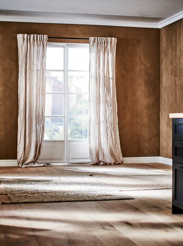 ห้องสีน้ำตาลและหน้าต่างสไตล์ French พร้อมผ้าม่านลินินที่มีรอยย่น และพรมจากวัสดุธรรมชาติสีน้ำตาลอ่อนบนพื้นไม้