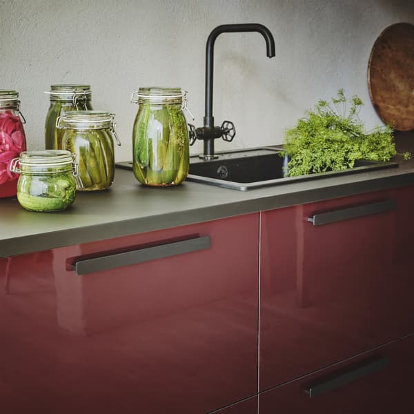 Frentes de cocina KALLARP de color marrón rojizo oscuro brillante con una encimera de color negro con tarros de comida en vinagre.