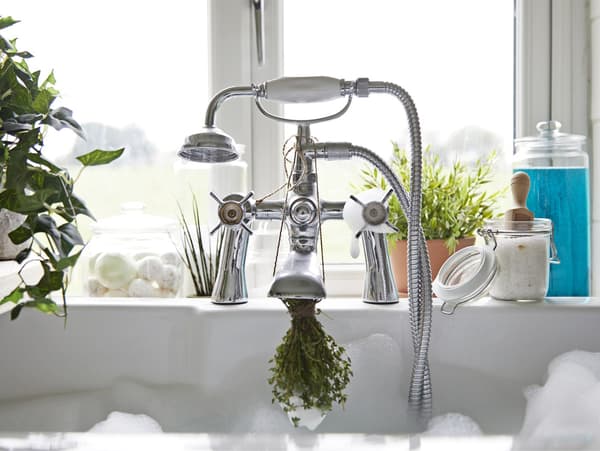 Fresh herbs tied to a running bath tap.