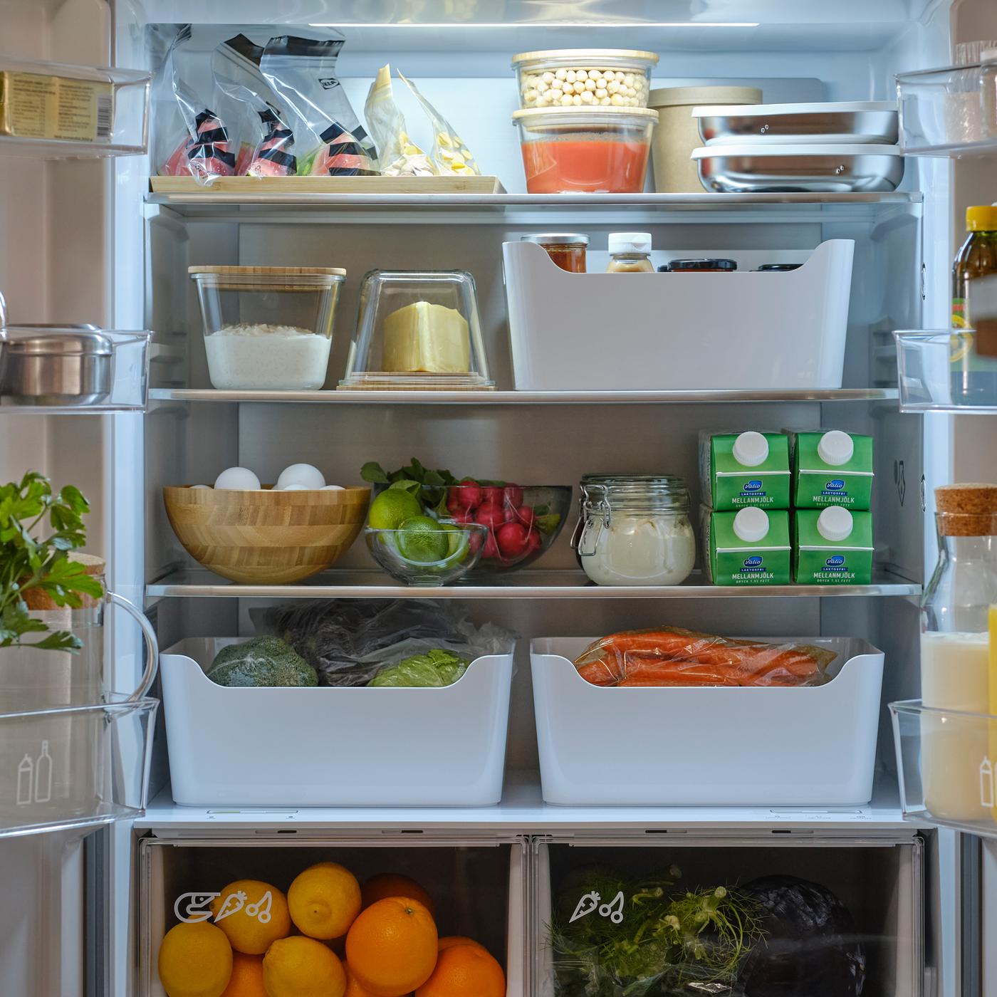 Frigorífico/congelador de porta dupla com as duas portas abertas a mostrar alimentos em recipientes, caixas, frascos, sacos reutilizáveis e uma garrafa de mesa.