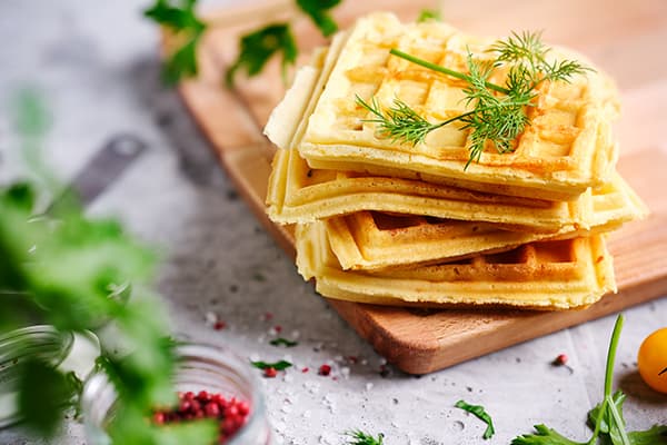 Frische vegetarische herzhafte Waffeln, die gerade aus dem Waffeleisen kommen, liegen auf einem Holzbrett.