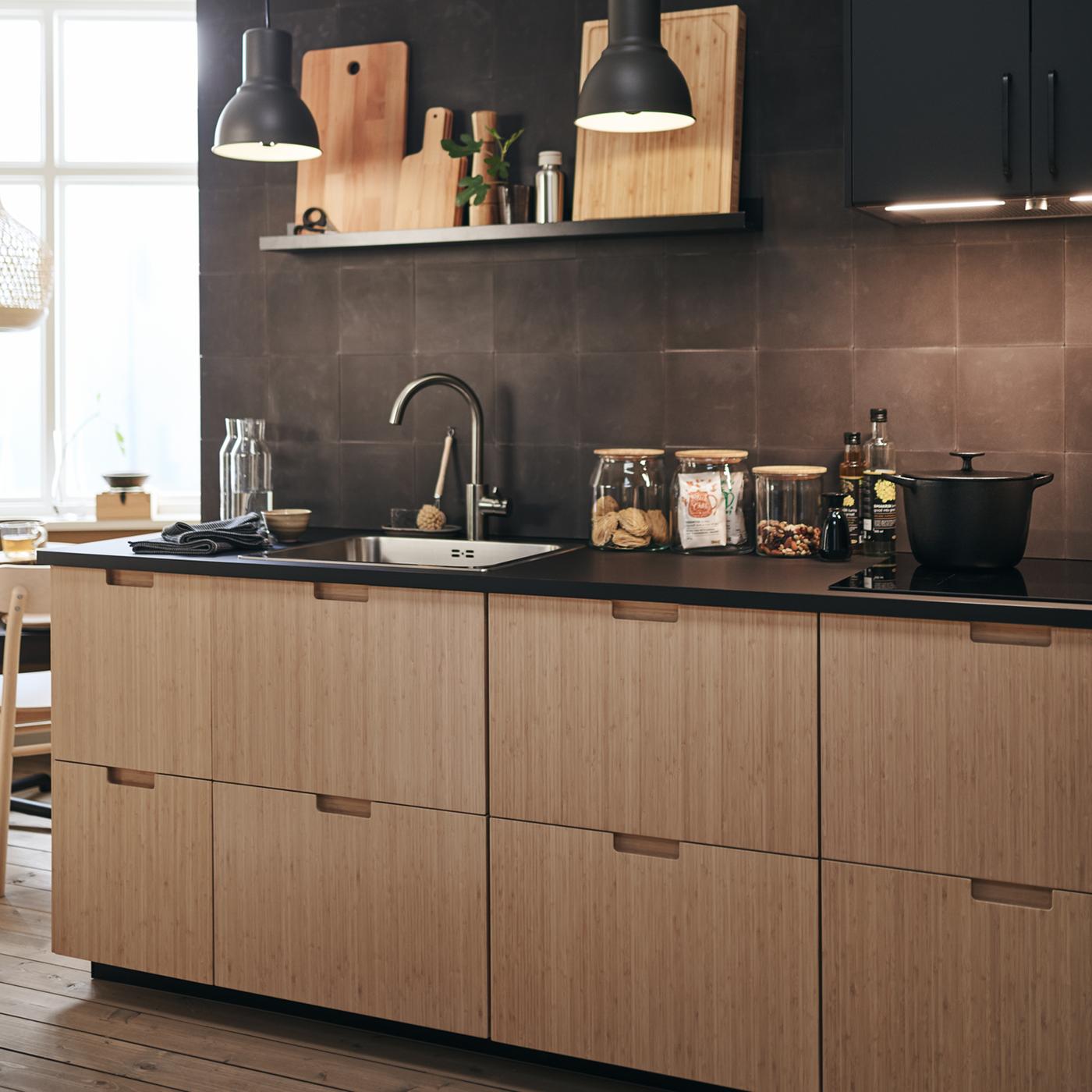 FRÖJERED kitchen fronts in bamboo, with diverse glass jars on the work surface and a cooking pot on the hob.