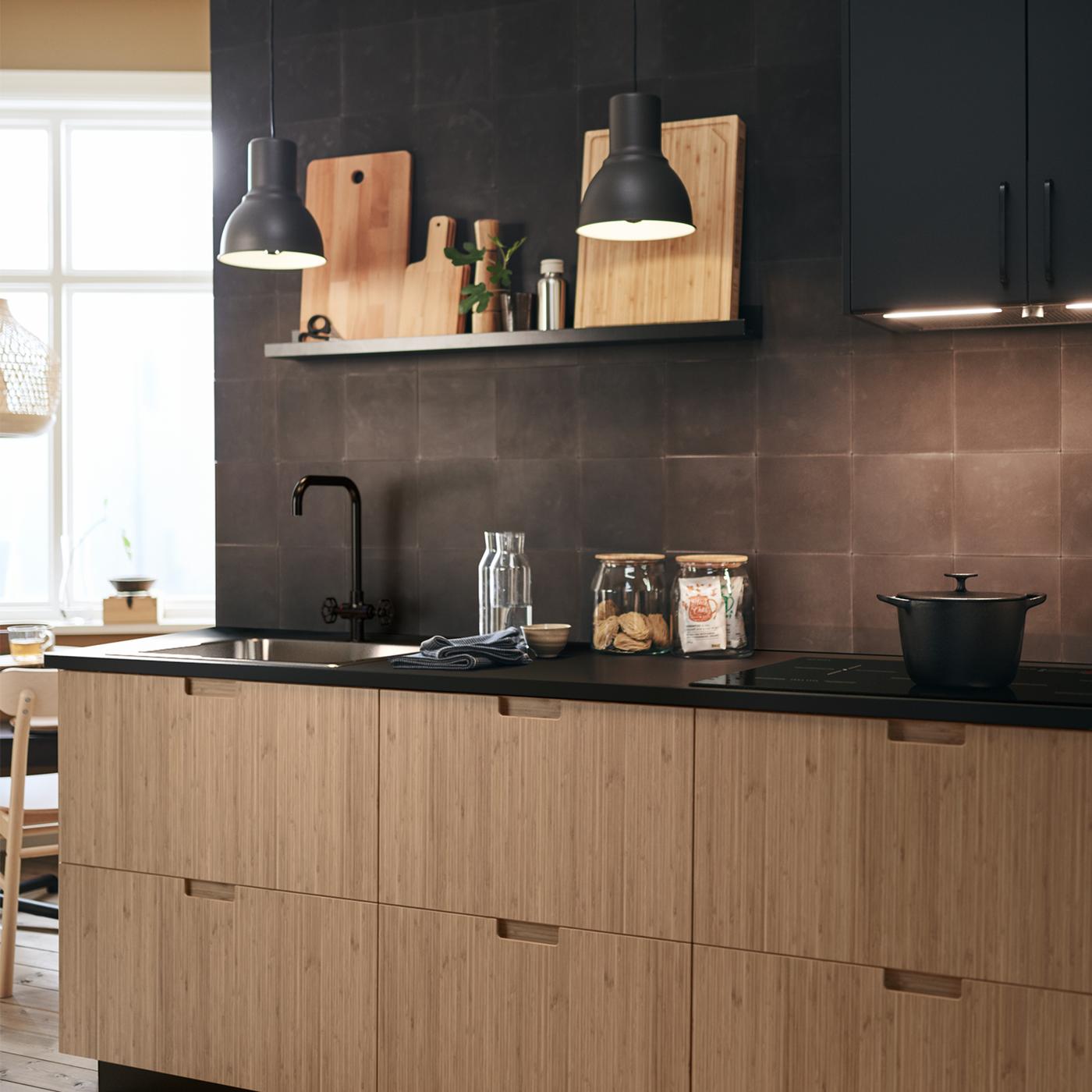 FRÖJERED kitchen fronts in bamboo, with diverse glass jars on the work surface and a cooking pot on the hob.