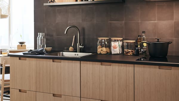 FRÖJERED kitchen fronts in bamboo, with diverse glass jars on the work surface and a cooking pot on the hob.