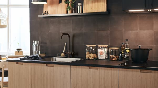 FRÖJERED kitchen fronts in bamboo, with various glass jars on the work surface and a cooking pot on the cooktop.