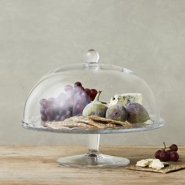Fromage, pain croquant et fruits dans un plat de présentation à couvercle en verre.