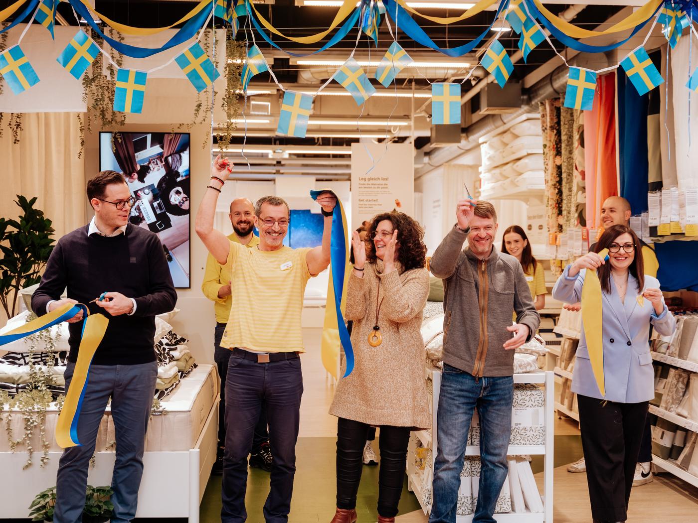 Fünf Personen stehen im neuen Schlafstudio und halten blau-gelbe Bänder in den Händen. Die Umgebung ist mit blau-gelben Fahnen und Girlanden dekoriert.