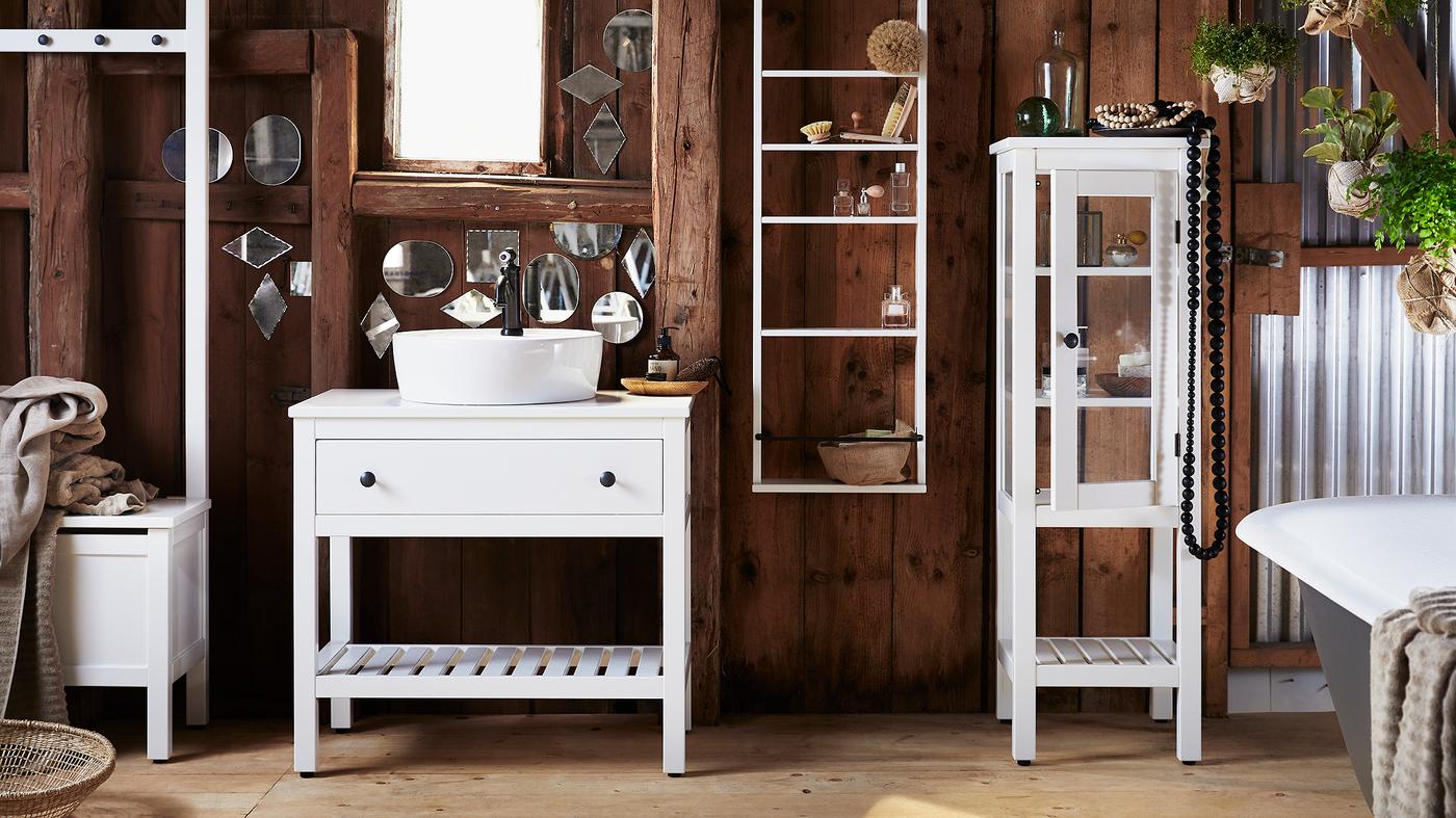 Fürdőszoba sötét fából készült falakkal, apró és furcsa alakú tükrökkel borítva, fehér HEMNES fürdőszobabútorokkal.