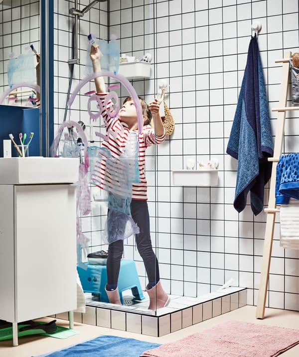 Fully clothed child, including rubber boots, standing in a dry shower, painting with watercolours on the glass partition.