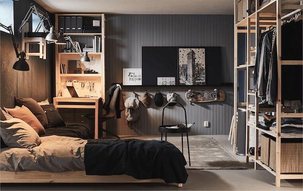 Fully furnished room with high windows, as in a basement or garage, with bed, desk and storage in various shelving units.