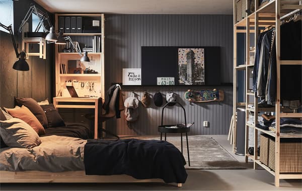 Fully furnished room with high windows, as in a basement or garage, with bed, desk and storage in various shelving units.