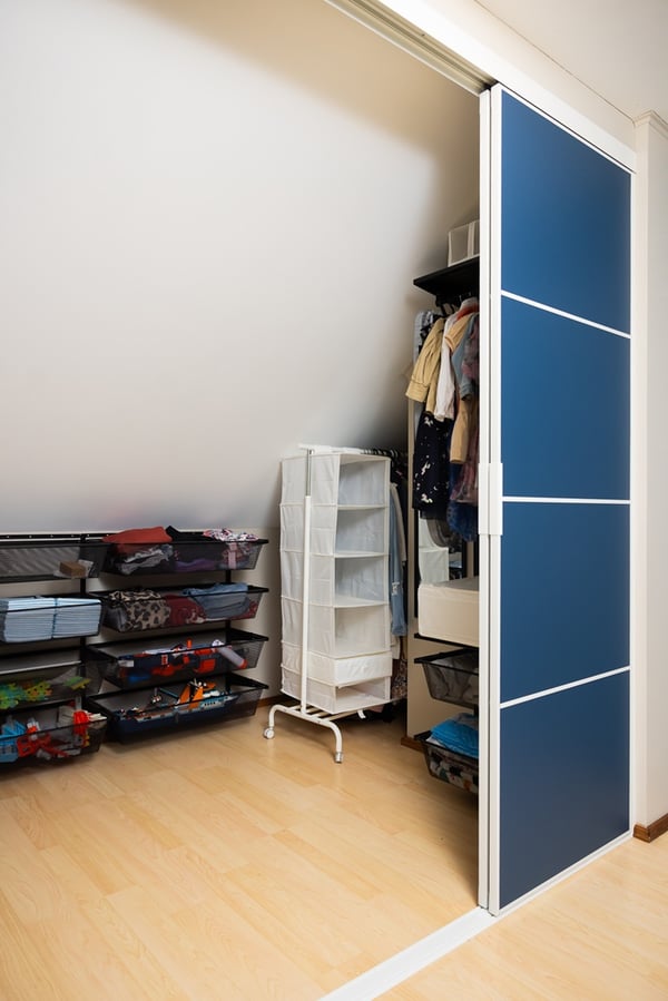 Fully opened wardrobe revealing shelves, drawers, hanging space, and clothing neatly organized in an attic storage area.