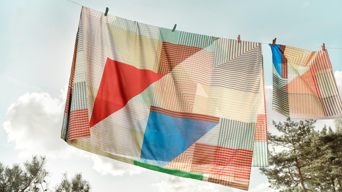 Fundas nórdica y de almohada PIMPERNÖT colgadas en un tendedero al aire libre con el cielo azul despejado de fondo.