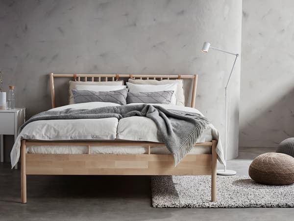 木製フレームのベッドにグレーの寝具を合わせたシンプルな寝室。コンクリート調の壁で落ち着いた雰囲気。