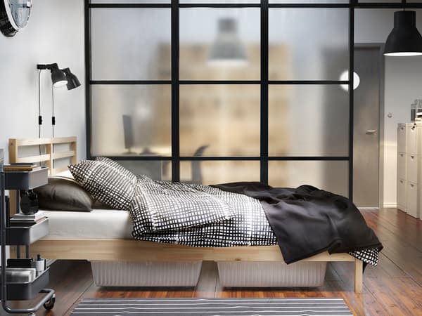 木製フレームのベッドにモノトーン寝具を合わせたシンプル寝室。黒いパーテーションでモダンな雰囲気。