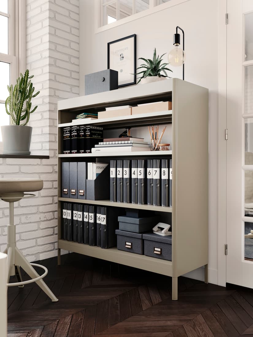 Gabinete IDÅSEN color beige, con varios documentos organizados. Sobre la estanteria hay decoración mural y de plantas. Al lado izquierdo se ve un piso y una macetera