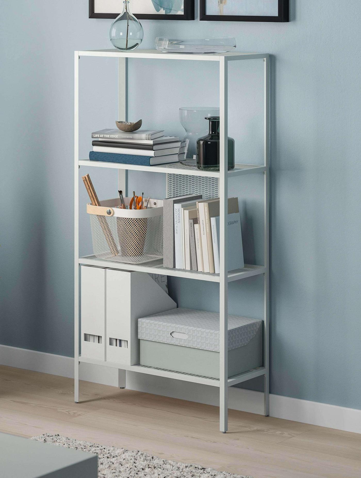 Gabinete IKEA BAGGEBO blanco con puertas de vidrio con libros y cajas decorativas en su interior.