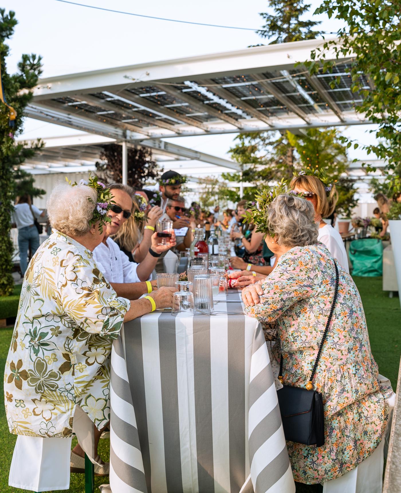 Gäste sitzen gemeinsam an einer festlich gedeckten Tafel und genießen das Midsommar-Event auf der IKEA Dachterrasse.