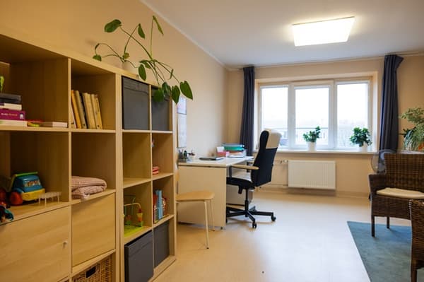 Gaiša istaba pirms interjera pārvērtībām ar dzeltenām sienām, atvērtiem plauktiem un darba galdu.