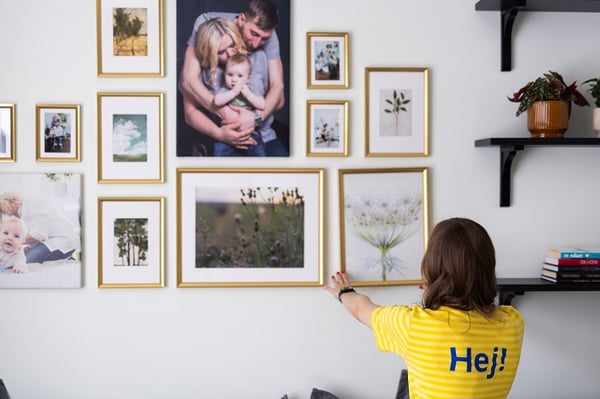 Gallery wall of framed family photos with woman adjusting artwork in cozy living room