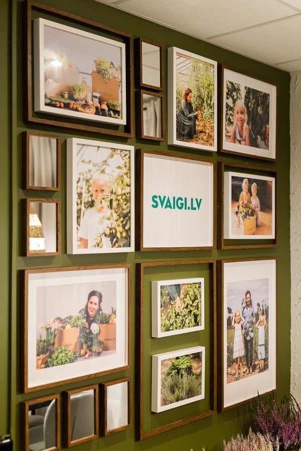Gallery wall of framed farm and family photos with SVAIGI.LV logo